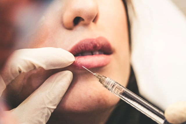 A medical professional administering botox injections to a woman’s lip for plumping purposes